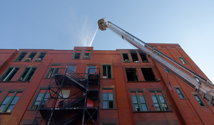 Above: On Friday, firefighters continued to spray water from above the collapsed roof in effort to douse stubborn flames. Below: By Monday, a fence had gone up around the building as the vacated structure continued to attract onlookers. Photos: Carl Glassman/Tribeca Trib